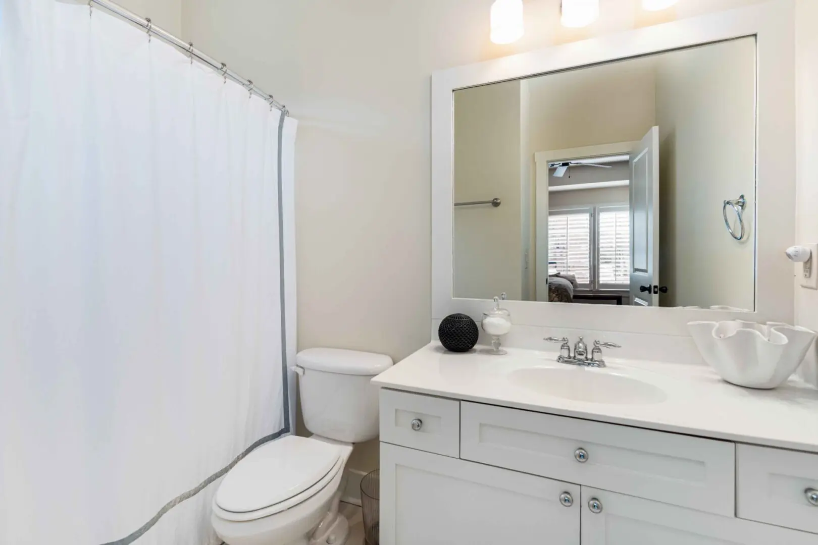 A bathroom with white walls and a toilet, sink, mirror, and shower.